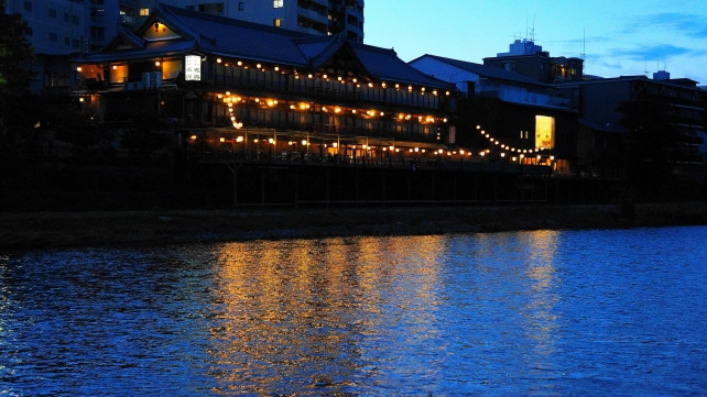鴨川の夕暮れ時に川面に反射する納涼床の灯り